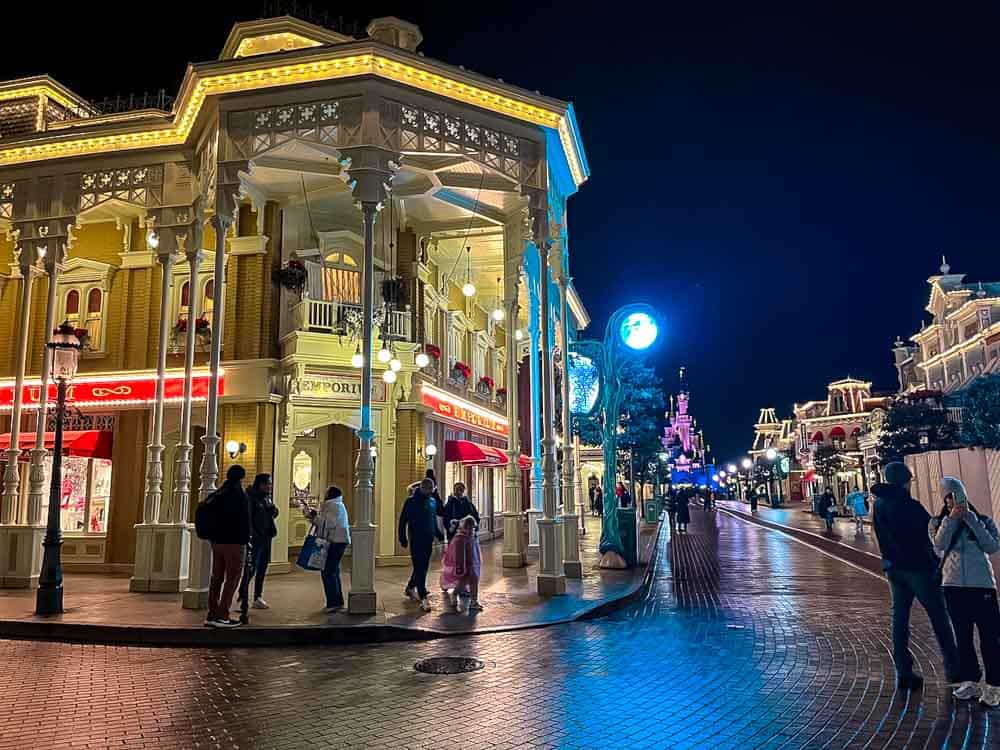 Main Street U.S.A. at Disneyland Paris at night in March, with wet pavements reflecting the lights and Sleeping Beauty Castle glowing in the distance