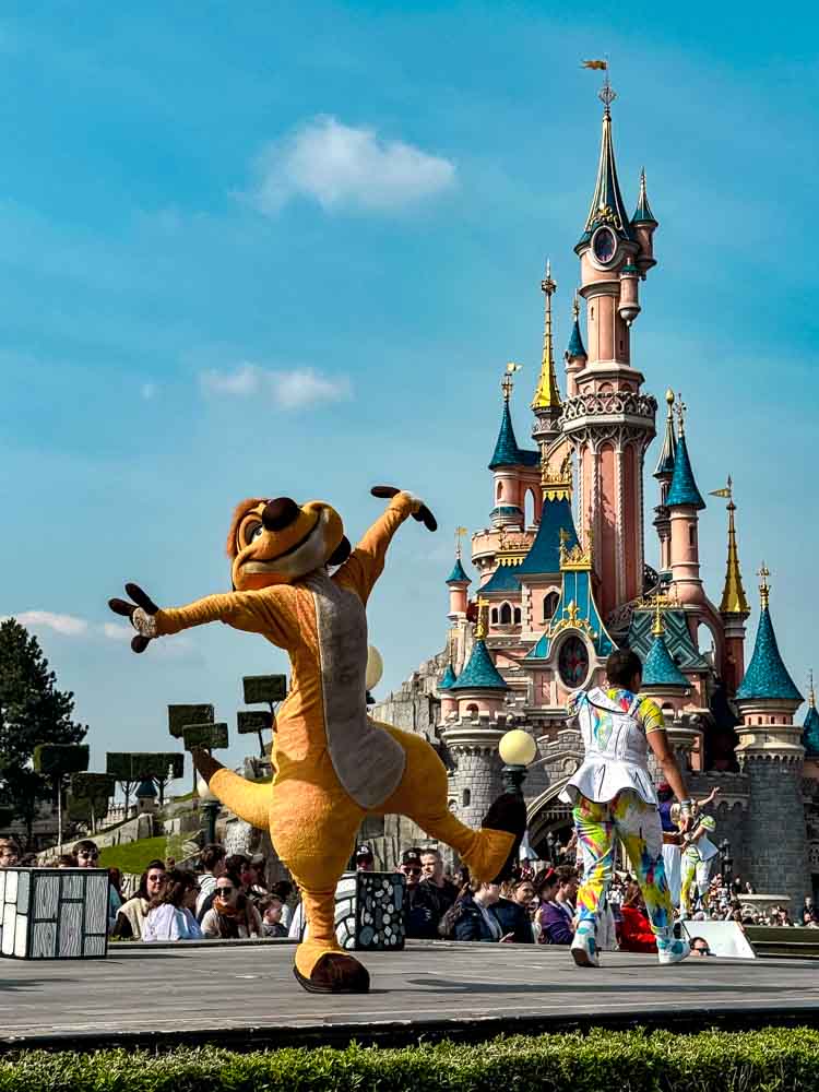 Timon performing in front of Sleeping Beauty Castle at Disneyland Paris during entertainment near Disney Adventure World worth it visit