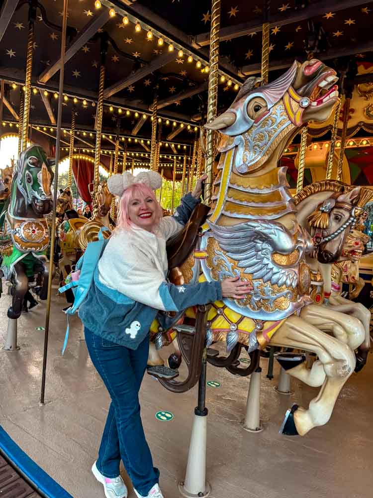 Woman posing with an ornate gold and silver carousel horse at Lancelot's Carousel, Disneyland Paris