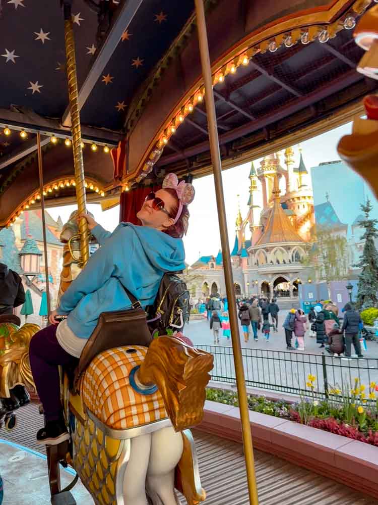 Woman seated on a carousel horse at Lancelot's Carousel, Disneyland Paris, with Sleeping Beauty Castle framed in the background