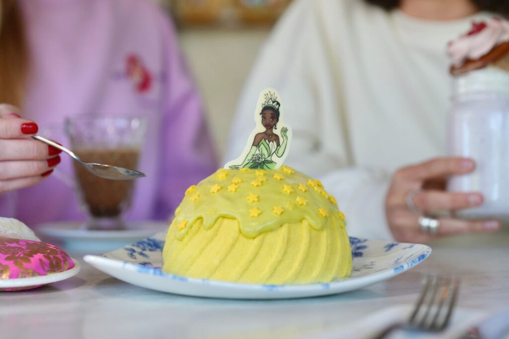 A yellow princess-dress-shaped dessert topped with a white chocolate Tiana decoration, served at Disneyland Paris during World Princess Week