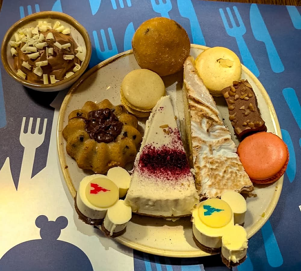 Plate of assorted Disneyland Paris buffet desserts including colourful macarons, cake slices, pastries and Mickey-shaped sweets.
