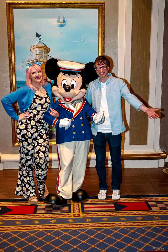 Carrie-Anne and her husband meeting Mickey Mouse, dressed in his captain’s outfit, in the lobby of Disney Newport Bay Club at Disneyland Paris, a hotel to consider when giving Disneyland Paris for Christmas.