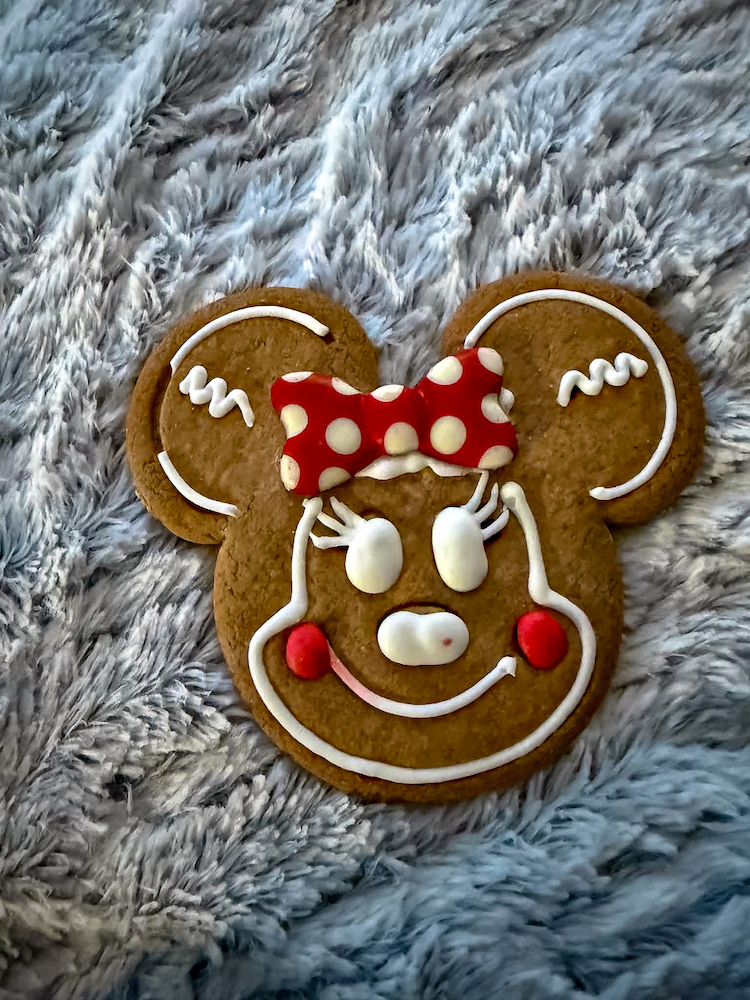 Large Minnie Mouse-shaped Christmas gingerbread biscuit decorated with white icing, red cheeks and a red polka-dot bow.