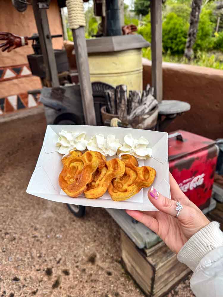Three golden Mickey Mouse-shaped waffles topped with whipped cream, served in a cardboard tray at Cool Post in Disneyland Paris.