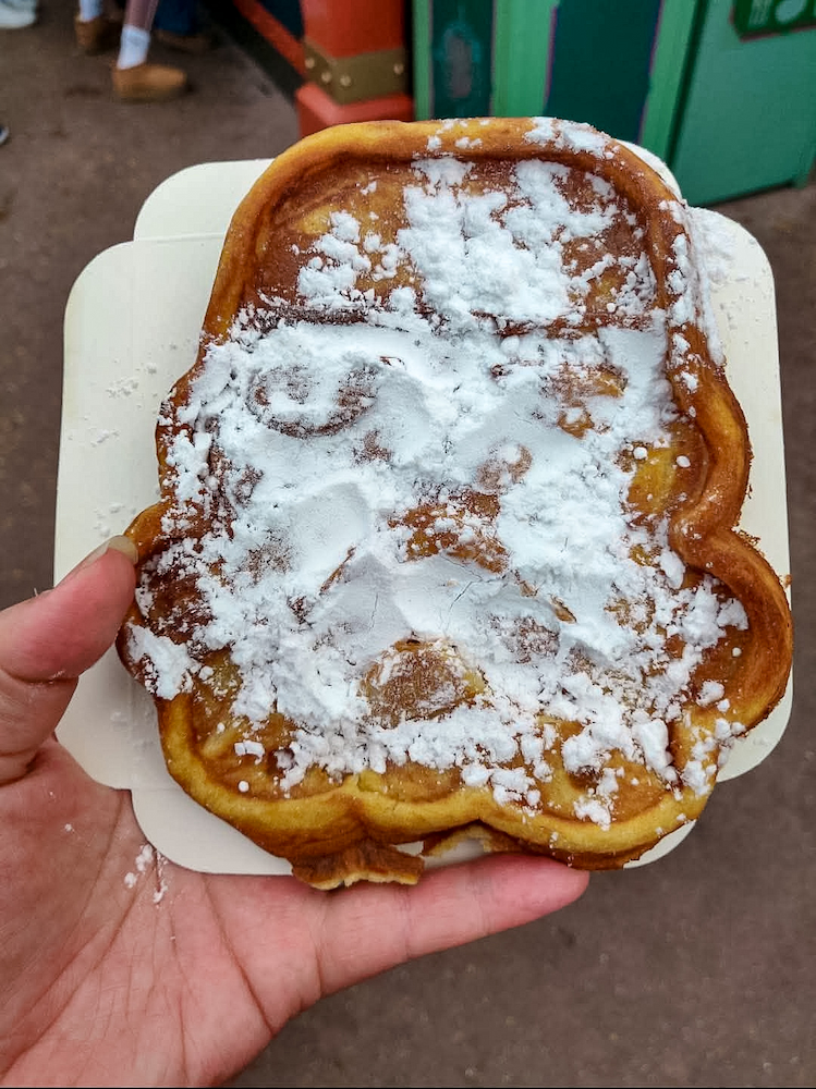 Large Stormtrooper-shaped golden waffle covered in powdered sugar and served in a cardboard tray at Disneyland Paris.
